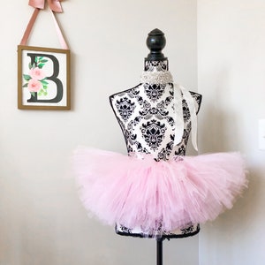 May include: A pink tulle tutu skirt on a black mannequin. The skirt is full and fluffy, and it is perfect for a ballerina or a princess.