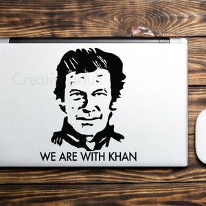 May include: Black and white sticker of a man's face with the text "WE ARE WITH KHAN" on a laptop.
