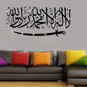 May include: Black and white wall decal with Arabic calligraphy and a sword design. The decal is displayed on a gray wall above a black leather couch with colorful throw pillows.