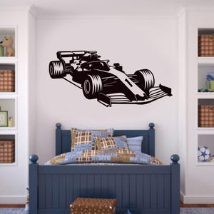 May include: Black and white silhouette of a racing car on a white wall. The car is facing the right side of the image. The car is in a bedroom setting with a bed and shelves in the background.