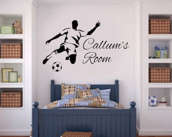 May include: Black and white silhouette of a soccer player kicking a ball with the text "Callum's Room" on a white wall. The wall is in a bedroom with a blue bed and a bookshelf.