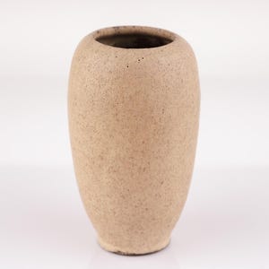 Könnte beinhalten: Eine kleine, beige Keramikvase mit einer strukturierten Oberfläche. Die Vase hat eine abgerundete, ovale Form.