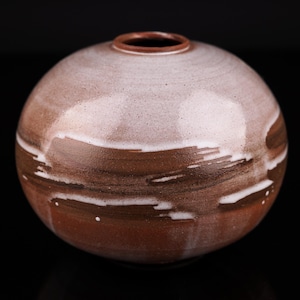 Peut inclure: Un vase rond en céramique brune avec un glaçage blanc et des stries brunes. Le vase a une finition lisse et brillante.