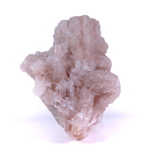 Puede incluir: Espécimen mineral de color rosa claro con una estructura cristalina. El mineral tiene una superficie rugosa y texturizada y un grupo de pequeños cristales en forma de aguja. El color es rosa pálido y suave, con algunas zonas más translúcidas.