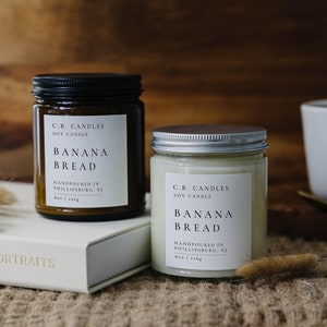 May include: Two soy candles in glass jars with brown and white labels. The labels read "C.B. Candles Soy Candle Banana Bread Handpoured in Phillipsburg, NJ 8oz | 226g".