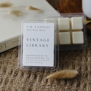 May include: A white wax melt in a clear plastic container with a label that reads "C.B. CANDLES SOY WAX MELT VINTAGE LIBRARY HANDPOURED IN PHILLIPSBURG, NJ 2.7 oz | 76.5 g"
