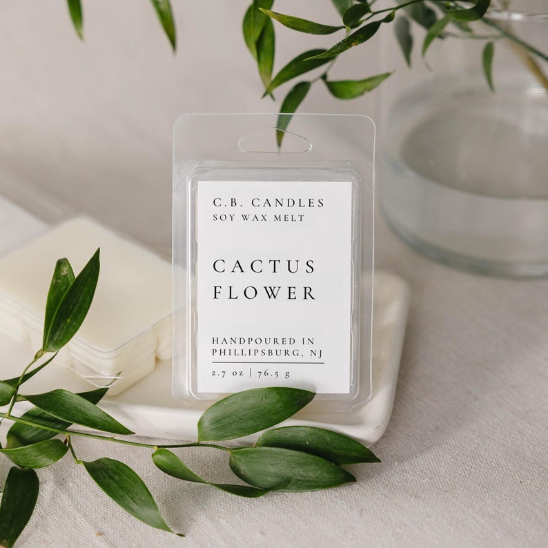 May include: A white soy wax melt in a clear plastic clamshell container. The label reads "C.B. CANDLES SOY WAX MELT CACTUS FLOWER HANDPOURED IN PHILLIPSBURG, NJ 2.7 oz | 76.5 g".