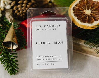 May include: A white label with black text reads "C.B. CANDLES SOY WAX MELT CHRISTMAS HANDPOURED IN PHILLIPSBURG, NJ 2.7 oz | 76.5 g". The label is in a clear plastic container.