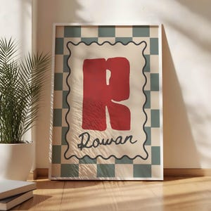 Puede incluir: Un póster enmarcado con la letra "R" roja y el nombre "Rowan" en cursiva. El diseño tiene un fondo crema, un borde ondulado y un patrón de cuadros verdes y blancos. El póster está enmarcado en un marco blanco.