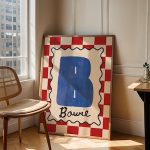 Könnte beinhalten: Ein gerahmter Kunstdruck mit einem großen blauen Buchstaben "B" mit weißen Linien auf cremefarbenem Hintergrund. Der Rand ist ein rot-weißes Schachbrettmuster. Das Wort "Bowie" steht unter dem Buchstaben.