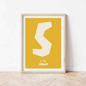 May include: A yellow poster with a white letter S and the text "S is for Sidonie".