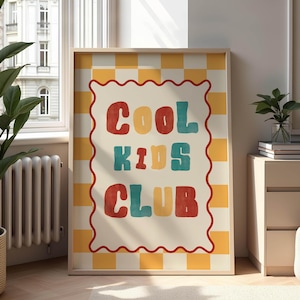 以下が含まれることがあります： 「COOL KIDS CLUB」の文字がカラフルなレトロスタイルで描かれたフレーム入りプリント。 赤、黄色、青の文字は、クリーム色の背景に赤い波型のボーダーと黄と白のチェック柄で配置されています。