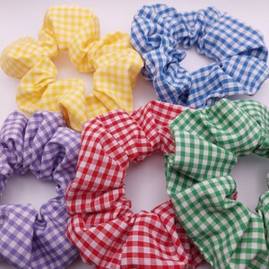 May include: Six fabric scrunchies in a variety of colours. The scrunchies are made from gingham fabric in yellow, blue, purple, red, and green. A popular hair accessory.