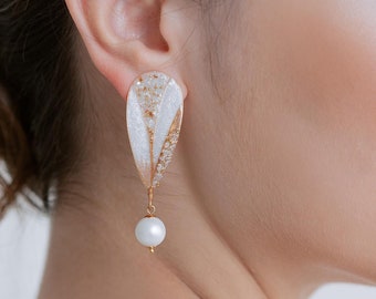 May include: Elegant, drop earrings with a pearlescent white and gold design. Each earring features a large, teardrop-shaped top with a dangling white pearl. The earrings are a sophisticated accessory.