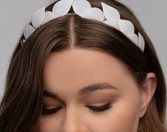 May include: A white headband with a petal design. The headband is made of a soft material and is worn on the head. The petals are evenly spaced around the band. The hair is long and brown.