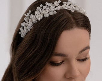 May include: A hair accessory featuring a delicate vine-like structure crafted from thin silver wire and small white beads. The piece is shaped into a flexible band that rests across the top of the head, showcasing intricate floral-inspired patterns.