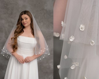 May include: A sheer, white bridal veil with delicate floral embellishments. The veil is adorned with small, white flowers, some featuring pearl centers. The veil is layered and drapes gracefully, creating a romantic and elegant look.