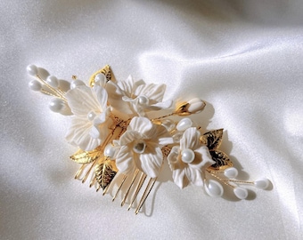 May include: A gold hair comb with white porcelain flowers and pearls. The comb is decorated with gold leaves and has a delicate design.