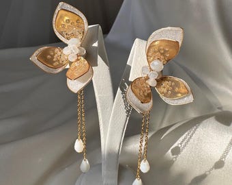 May include: Elegant gold and white butterfly earrings with a layered design. The earrings feature a gold chain with white teardrop-shaped beads. The butterfly wings have a gold and white color scheme, creating a sophisticated and eye-catching accessory.