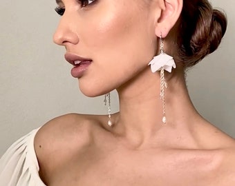 May include: Elegant white floral drop earrings with delicate chain and pearl accents. The earrings feature a layered petal design and are suspended from a silver hook. The earrings are a beautiful accessory for special occasions.