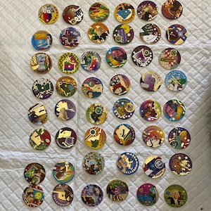May include: A collection of 50 colorful round tokens featuring state symbols and names. Each token has a gold-colored rim and a unique design representing a different state in the United States.