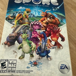 May include: A Spore video game box featuring various colorful alien creatures against a blue and green background. The game title is in large white letters. The box also includes the ESRB rating, Win/Mac compatibility, and the EA logo.