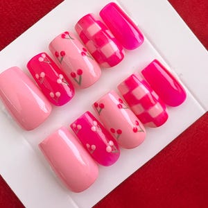 May include: Set of pink and white press-on nails with cherry and checkered designs.