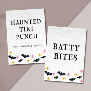 May include: Two white rectangular signs with black text and Halloween-themed graphics. One sign reads "HAUNTED TIKI PUNCH" with "RUM PINEAPPLE SPRITE" below. The other says "BATTY BITES". Both have bats and stars.