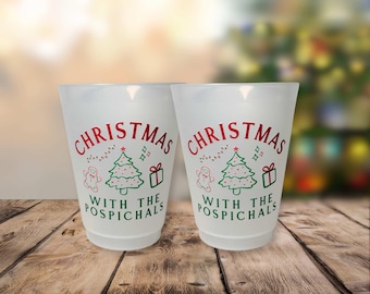 May include: Two white plastic cups with a festive Christmas design. The cups display the text "CHRISTMAS WITH THE POSPICHALS" in red, along with a Christmas tree, gingerbread man, and gift illustrations.