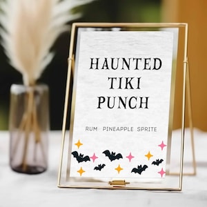 May include: A gold framed sign with the words "HAUNTED TIKI PUNCH" in black. The sign also says "RUM PINEAPPLE SPRITE" below the title. The bottom of the sign has black bats, pink stars, and orange stars.