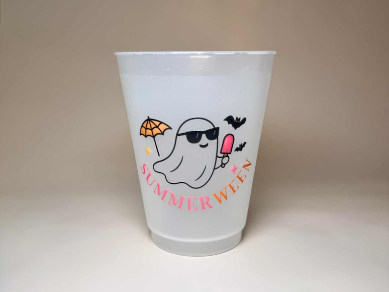 May include: A translucent plastic cup with a "Summerween" design. The design features a cartoon ghost wearing sunglasses and holding a popsicle, with an orange umbrella and bats. The text "Summerween" is in pink and orange.