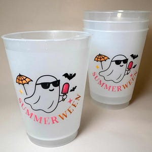 May include: Two white plastic cups with a cartoon ghost wearing sunglasses, holding a popsicle, and an umbrella. The cups have the word "SUMMERWEEN" in pink and orange. Bats and stars are also included in the design.