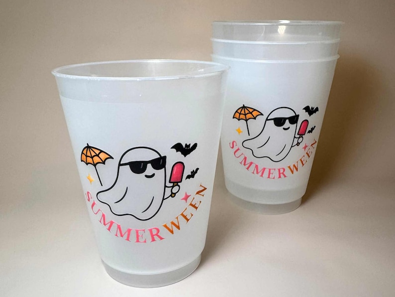 May include: Two white plastic cups with a cartoon ghost wearing sunglasses, holding a popsicle, and an umbrella. The cups have the word "SUMMERWEEN" in pink and orange. Bats and stars are also included in the design.