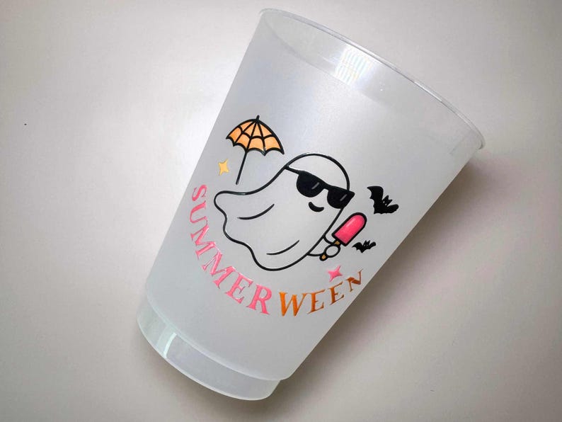May include: A clear plastic cup with a "Summerween" design. The design features a ghost wearing sunglasses, holding a popsicle, and an umbrella. The text "Summerween" is in pink and orange.