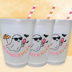 May include: Three white plastic cups with a ghost graphic wearing sunglasses and holding a popsicle. The cups have the word "SUMMERWEEN" in pink and are decorated with bats and an umbrella. Each cup has a striped straw.