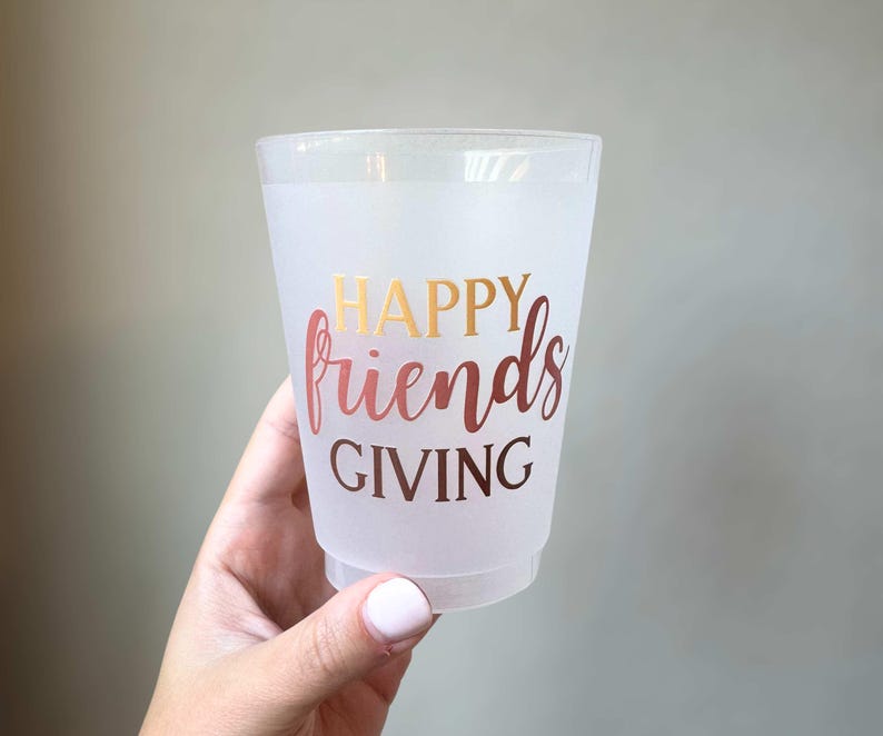 Peut inclure: Un gobelet en plastique transparent avec les mots "HAPPY friends GIVING" en lettres dor&eacute;es et or rose. Le gobelet est tenu par une main avec du vernis &agrave; ongles rose clair.