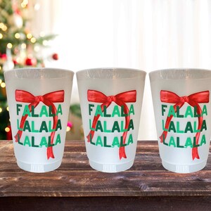 以下が含まれることがあります： 赤と緑のクリスマスデザインが施された白いプラスチック製のカップが3つあります。カップには「Falala Lalala Lalala」と印刷されています。