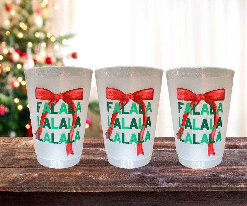 以下が含まれることがあります： 赤と緑のクリスマスデザインが施された白いプラスチック製のカップが3つあります。カップには「Falala Lalala Lalala」と印刷されています。