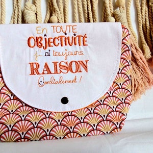 May include: White zippered pouch with a pink and gold geometric pattern. The pouch has a white flap with the text "En toute objectivit&eacute; j'ai toujours RAISON Cordialement!" embroidered in orange.