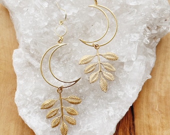 May include: Gold crescent moon earrings with a delicate leaf design and clear crystal accents.