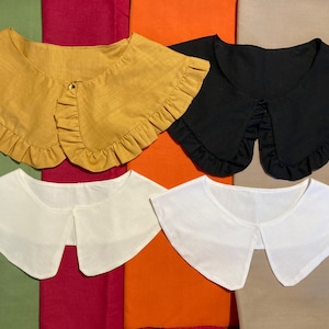 May include: Four different fabric collars with ruffled edges. The collars are in yellow, black, white, and white. The collars are laid out on a multi-coloured fabric background.