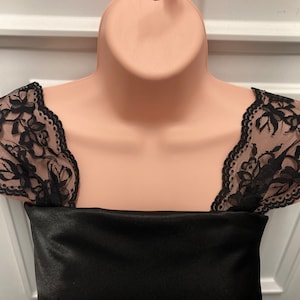 May include: A black satin top with black lace trim around the neckline. The lace has a floral pattern.