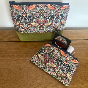 May include: Two zippered pouches with a floral pattern featuring birds and a green background. The larger pouch has a solid green bottom. The smaller pouch is open and has a small mirror and a makeup brush inside.