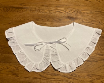 May include: White cotton collar with a ruffled edge and a white ribbon tied in a bow at the centre.