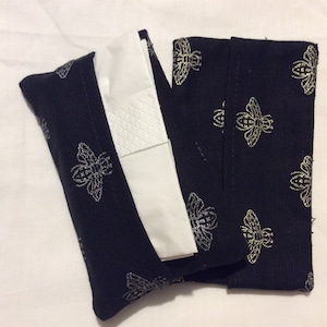 Peut inclure: Boîte à mouchoirs en tissu noir avec un motif d'abeilles dorées. Le couvercle est plié et contient une boîte de mouchoirs blancs.