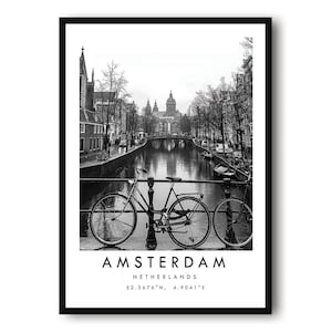 May include: A black and white framed wall art print featuring a bicycle parked on a bridge overlooking an Amsterdam canal. The text at the bottom reads AMSTERDAM NETHERLANDS 52.3676° N, 4.9041° E in a clean, sans-serif font on a white background.