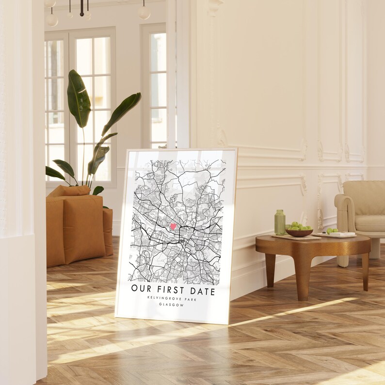 A framed map of Glasgow, Scotland, with the text "Our first date" and "Glasgow" printed on it, is displayed in a living room with a wooden floor and a beige sofa.