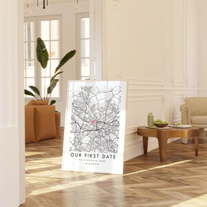 A framed map of Glasgow, Scotland, with the text "Our first date" and "Glasgow" printed on it, is displayed in a living room with a wooden floor and a beige sofa.