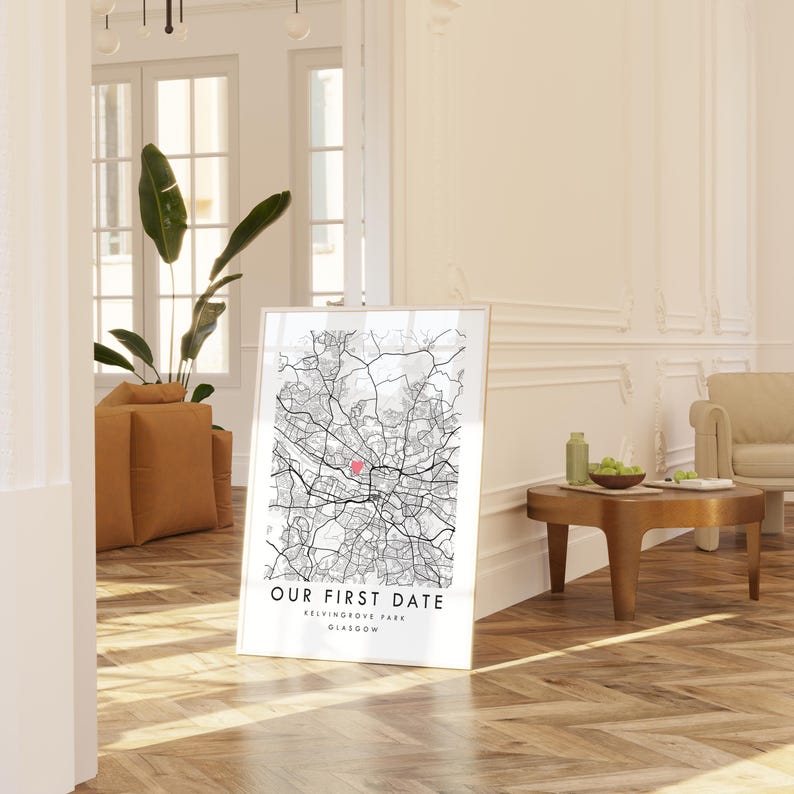 A framed map of Glasgow, Scotland, with the text "Our first date" and "Glasgow" printed on it, is displayed in a living room with a wooden floor and a beige sofa.