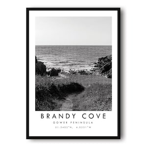 Könnte beinhalten: Schwarz-Weiß-Druck von Brandy Cove, Gower Peninsula, in einem Rahmen. Das Bild zeigt eine Küstenlandschaft mit einem Pfad, der zum Meer führt. Der Text "Brandy Cove" und Koordinaten sind unten im Rahmen aufgedruckt.
